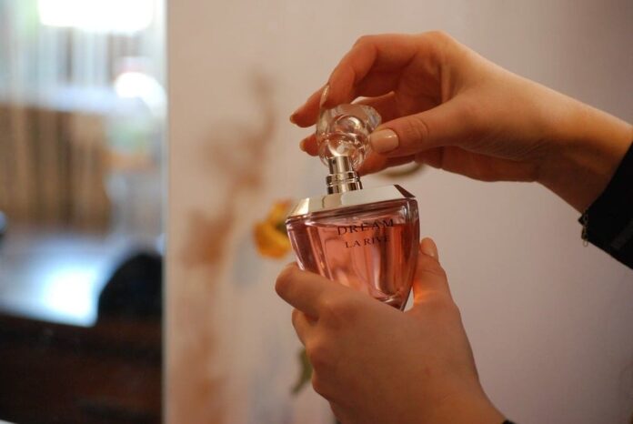 Fotografia de mãos femininas segurando um frasco de perfume, utiliza para ilustrar artigo sobre como passar perfume corretamente.