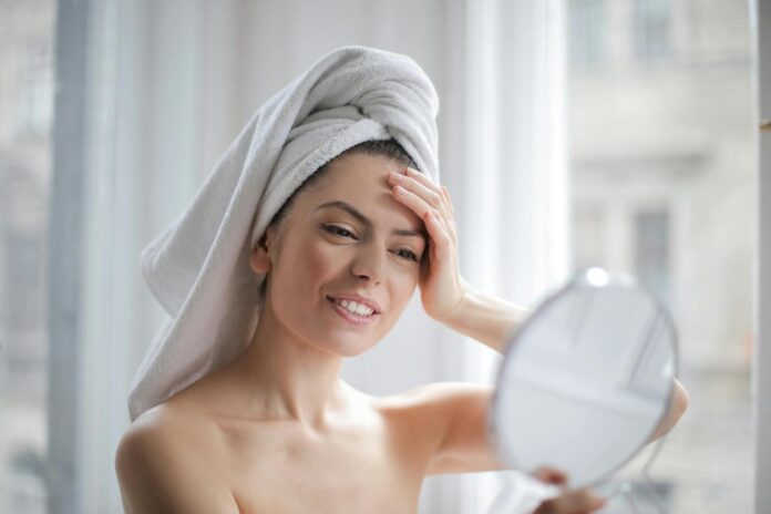 melhor ácido para manchas - foto de capa Fotografia de moça fazendo skincare em frente ao espelho, utilizada para ilustrar artigo sobre o melhor ácido para manchas.